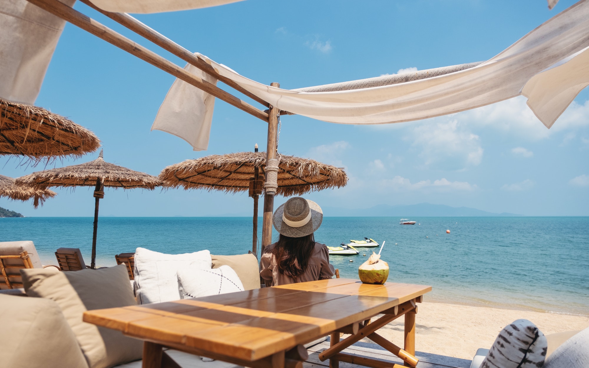 Rear view image of a woman looking at a beautiful sea while sitting in the cafe on the beach